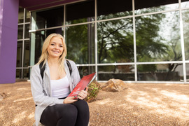 Girl in a grey shirt sitting outside the student union on the Sierra Vista Campus