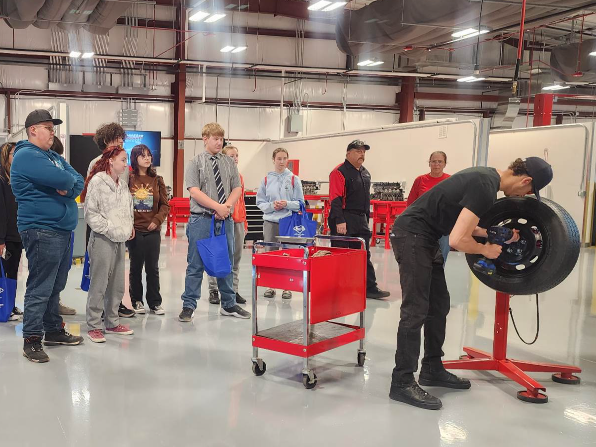 High School students watching an automotive instructor fix a tire